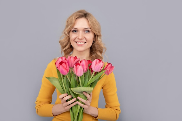 La ragazza positiva tiene i fiori per le vacanze primaverili su sfondo grigio