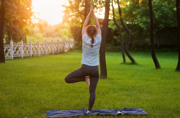 La ragazza pratica lo yoga nel parco su un prato verde.