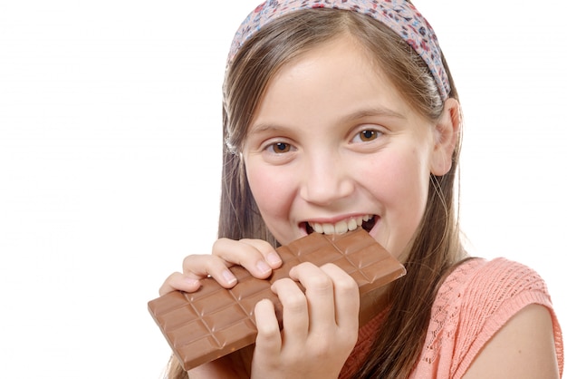 La ragazza pre teenager mangia il cioccolato, isolato su bianco