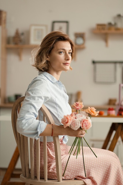 La ragazza premurosa con i fiori nelle sue mani si siede su una sedia in cucina