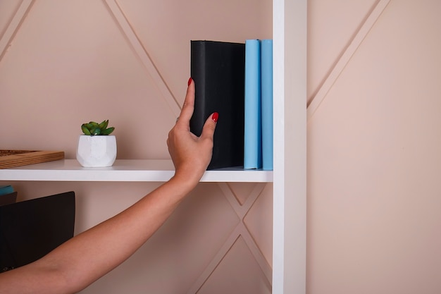 La ragazza prende un libro con una copertina nera da uno scaffale bianco