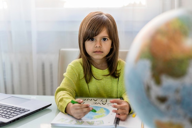 La ragazza preoccupata del bambino disegna il pianeta terra con i colori della cera sul taccuino della scuola per la giornata della Terra La piccola ragazza attivista scrive il messaggio Salva il pianeta Protezione dell'ambiente e concetto di riscaldamento globale