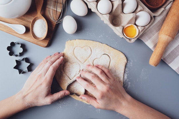 La ragazza prepara i biscotti a forma di cuore, composizione piatta laica su uno sfondo grigio.