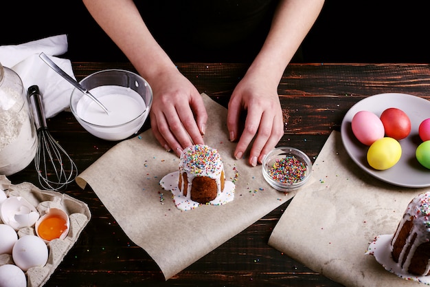 La ragazza prepara la cottura pasquale, spalma la torta con glassa e spruzza con polvere colorata