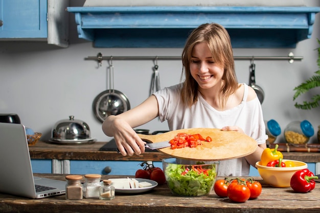 La ragazza prepara un'insalata vegetariana in cucina aggiunge gli ingredienti a fette al piatto