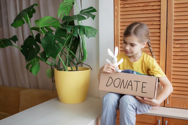 La ragazza raccoglie i vestiti per la scatola delle donazioni a casa. Tiene in mano un giocattolo da aggiungere. L'attivismo della moda di seconda mano e circolare, il concetto di aiuto e supporto, salva l'inquinamento del pianeta.