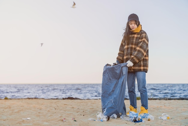 La ragazza raccoglie l'immondizia di plastica in un sacco dell'immondizia sulla spiaggia sabbiosa