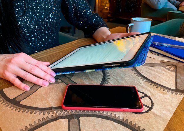 La ragazza ravvicinata sta lavorando o studiando in un bar con un tablet, un telefono e un notebook nelle vicinanze. Coworking, organizzazione del flusso di lavoro. Concetto di affari o di istruzione.