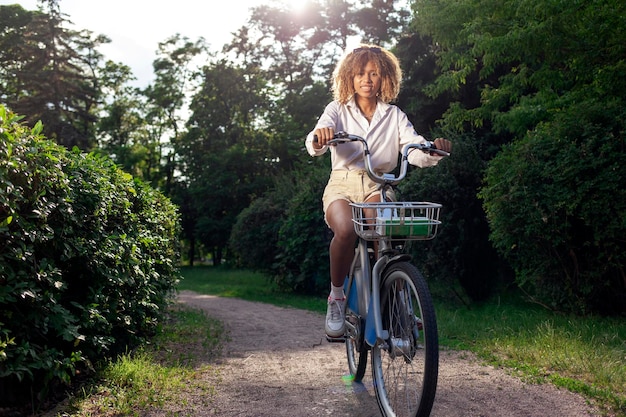 La ragazza riccia afroamericana va in bicicletta nel parco in estate e distoglie lo sguardo dallo spazio della copia