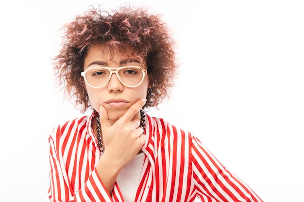 La ragazza riccia divertente che tiene il suo mento pensa che i dubbi prendano una decisione isolata su sfondo bianco per studio