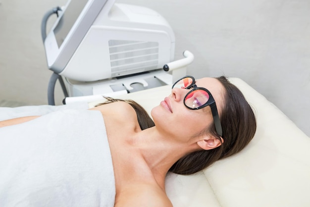 La ragazza rilassata è sdraiata sul lettino da massaggio con serenità Indossa occhiali protettivi per la procedura laser