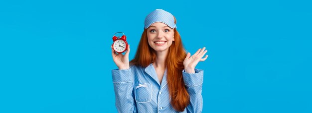 La ragazza rossa allegra ed entusiasta non vuole dormire troppo imposta la sveglia con l'orologio rosso e