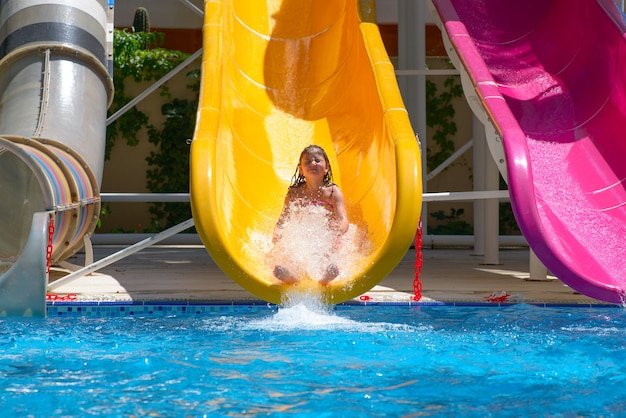 La ragazza rotola giù per gli scivoli d'acqua al parco acquatico