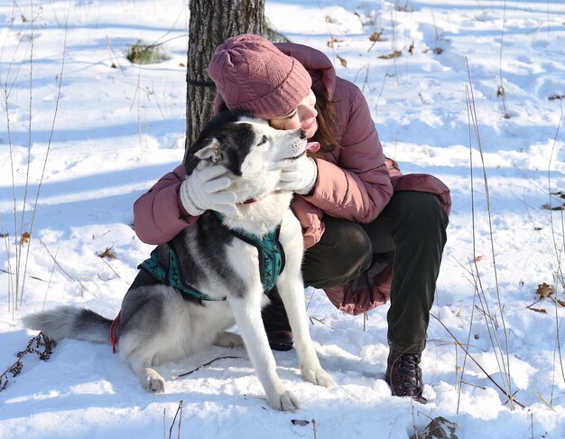 La ragazza russa si è aggrappata amorevolmente al husky siberiano sullo sfondo invernale nella foresta
