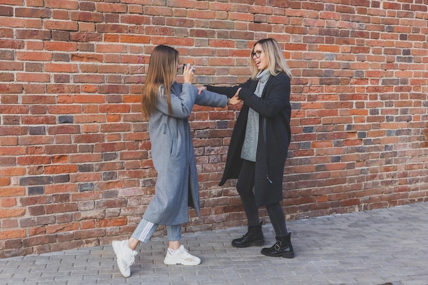 La ragazza scatta una foto della sua amica davanti al muro di mattoni nel concetto di fotografo di strada urbano e stile di vita urbano giovanile
