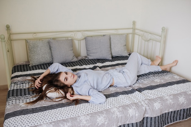 La ragazza sdraiata in pigiama sul letto nella sua stanza. Elegante interno grigio-bianco.