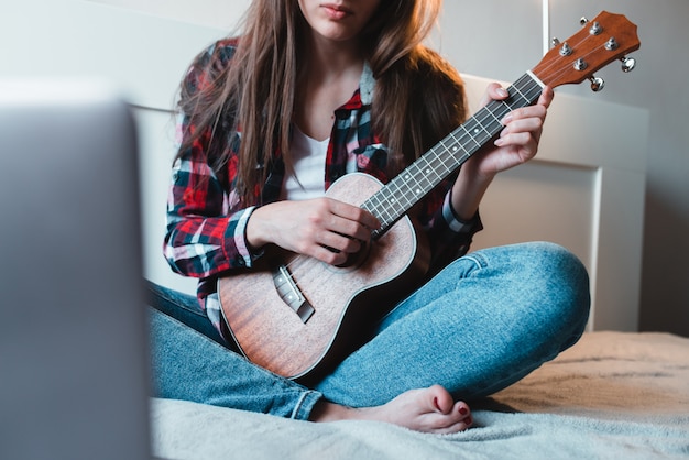 La ragazza seduta a casa impara a suonare le ukulele usando le lezioni online.