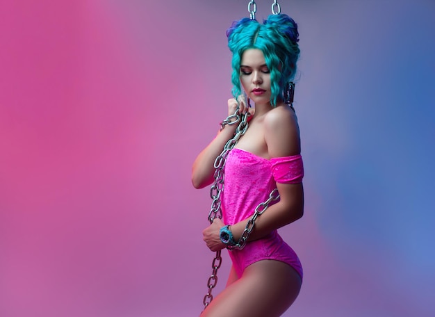 La ragazza sexy con i capelli colorati in un body rosa acceso con una catena di metallo su sfondo neon