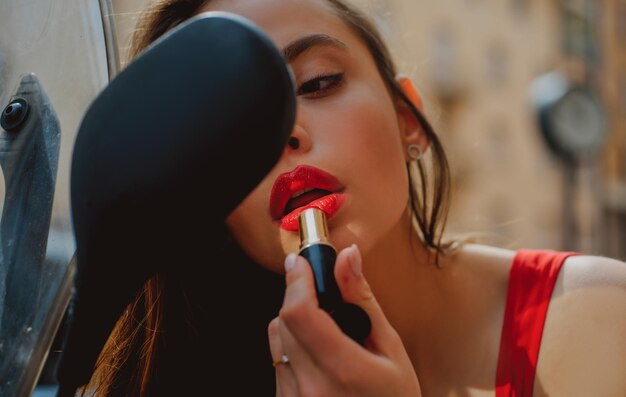 La ragazza sexy di moda di vita di città con le labbra rosse mette il rossetto che guarda in uno specchio della moda della strada del motociclo