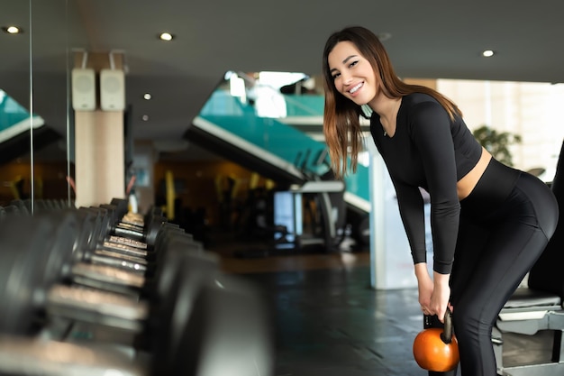 La ragazza si accovaccia con manubri e sorride Giovane sportiva allena le gambe in palestra Stile di vita sano