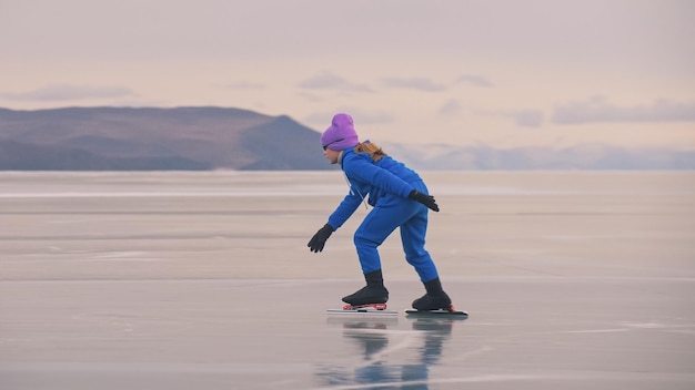 La ragazza si allena sul pattinaggio di velocità sul ghiaccio. Il bambino pattina in inverno in tuta sportiva blu, occhiali sportivi. Sport di pattinaggio di velocità per bambini.