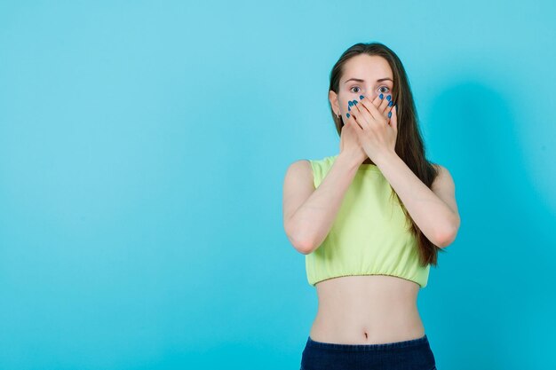 La ragazza si copre la bocca con le mani su sfondo blu