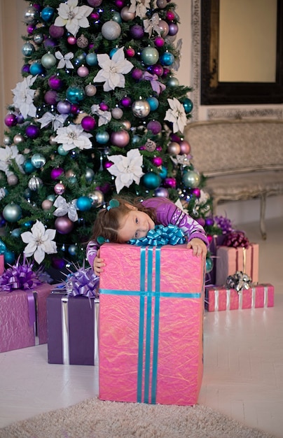 La ragazza si è sdraiata su un enorme regalo rosa di Capodanno Dietro c'è un bellissimo albero di Natale