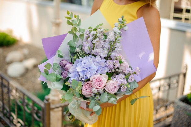 La ragazza si è vestita in un vestito giallo che tiene un mazzo viola dei fiori