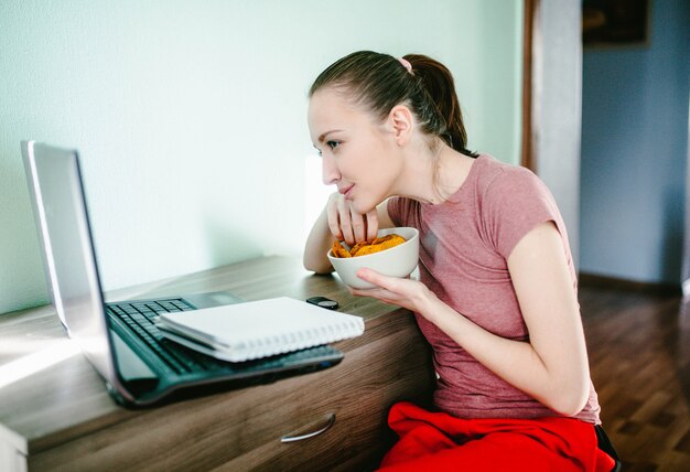 La ragazza si siede ad un laptop con le patatine fritte