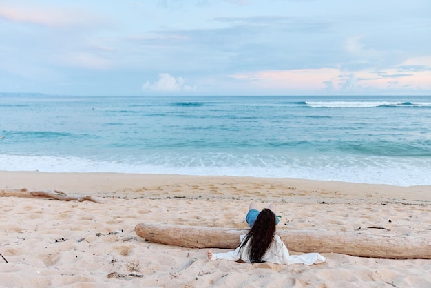 La ragazza si siede con le spalle alla telecamera sulla sabbia della spiaggia e guarda l'oceano durante una gita sull'isola rilassando la salute mentale