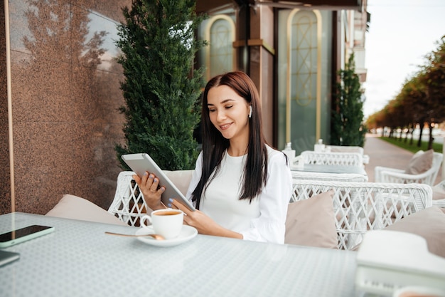 La ragazza si siede in un caffè usando la tecnologia. la ragazza guarda un teleon in un caffè a un tavolo.