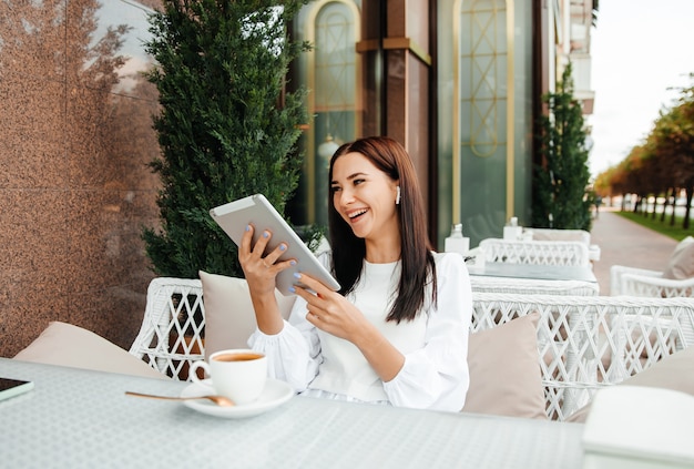 La ragazza si siede in un caffè usando la tecnologia. la ragazza guarda un teleon in un caffè a un tavolo.