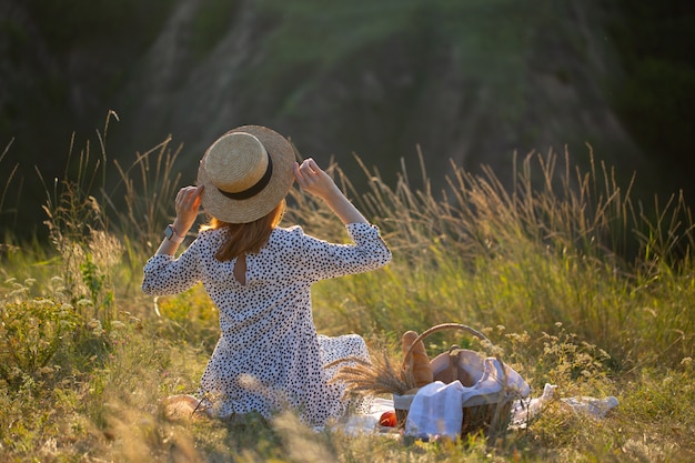 La ragazza si siede nell'erba in natura. La ragazza guarda il tramonto. La ragazza sta riposando in natura con un cesto di cibo. Picnic in natura.