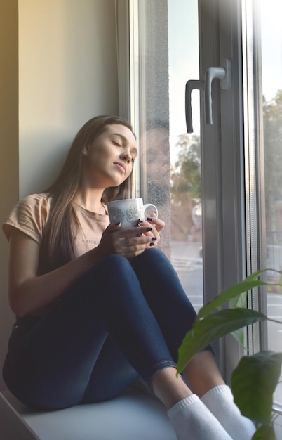 la ragazza si siede sul davanzale e beve il caffè