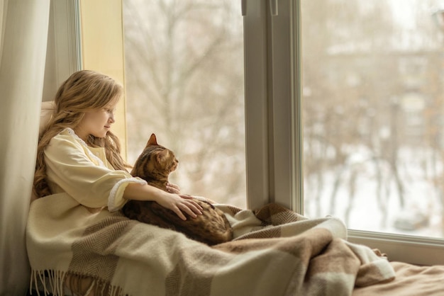 La ragazza si siede sul davanzale vicino alla finestra con un gatto