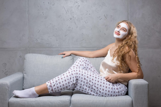 La ragazza si siede sul divano indossando una maschera cosmetica.