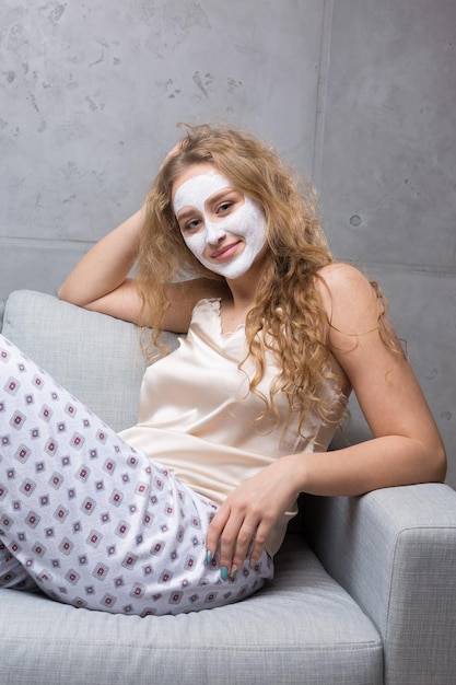 La ragazza si siede sul divano indossando una maschera cosmetica.