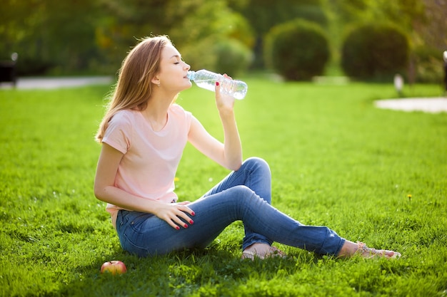 La ragazza si siede sul prato e beve l'acqua