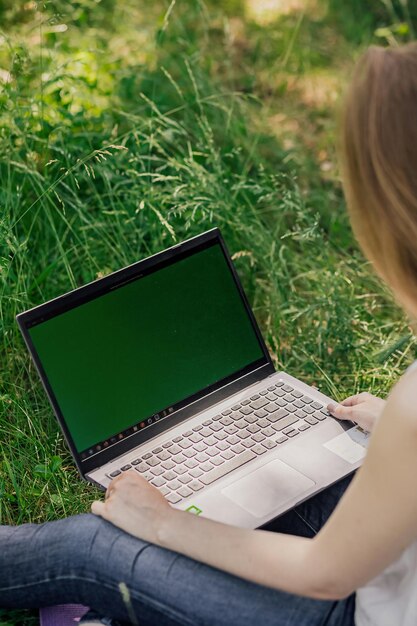 La ragazza si siede sull'erba e lavora in un computer portatile freelance di autoeducazione il concetto di apprendimento a distanza all'aperto