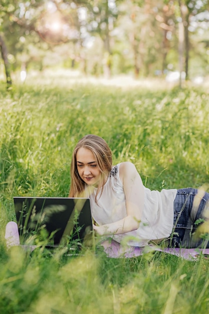 La ragazza si siede sull'erba e utilizza un computer portatile Concetto di tecnologia per lo stile di vita educativo Concetto di apprendimento all'aperto