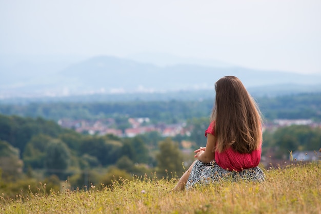 La ragazza si siede sulla montagna e guardando la valle con la cittadina e le montagne