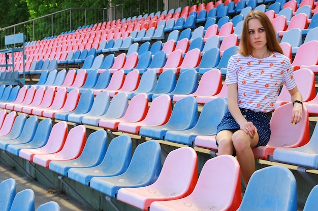 La ragazza si siede sulle panchine dello stadio e guarda il calcio sull'erba È preoccupata per la partita