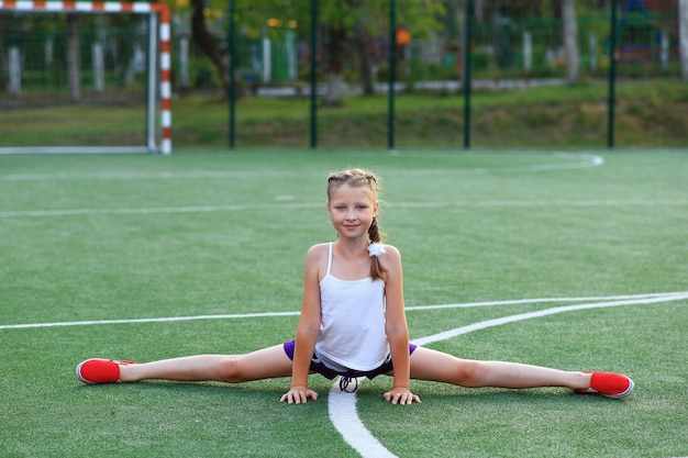 La ragazza si siede sullo spago sul campo sportivo.