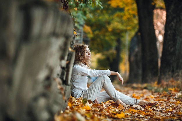 La ragazza si siede tra le foglie d'autunno