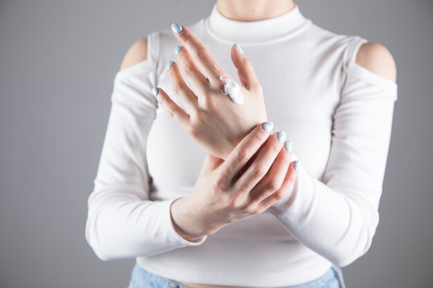 La ragazza si strofina le mani con la crema su una scena grigia