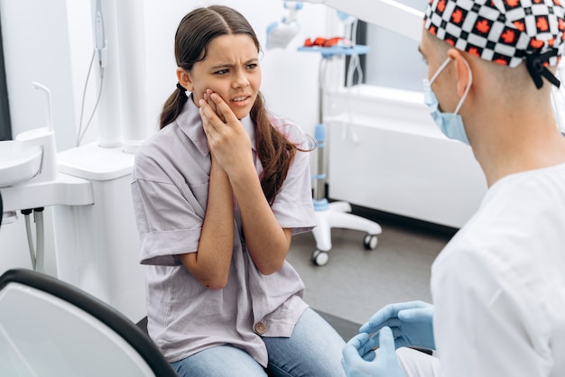 La ragazza si tocca le guance con la mano. Una ragazza carina e storta dice al dentista che ha mal di denti.