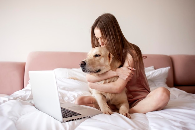 La ragazza si trova sul letto con il cane golden retriever e usa il computer portatile libero professionista femminile con l'animale domestico