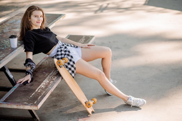 La ragazza skater adolescente e uno skateboard si sta rilassando sulla panchina nel parco dei pattinatori
