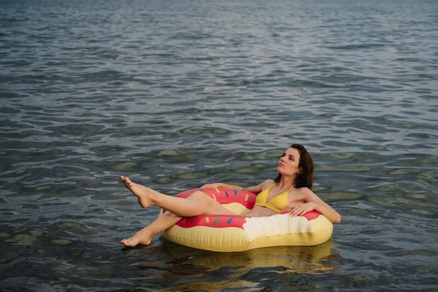 La ragazza snella nuota su un cerchio gonfiabile in mare in estate in vacanza