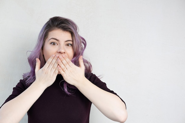 La ragazza sorpresa con i capelli viola si copre la bocca con le mani. Spazio per il testo